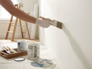 Professionele schilder past witte verf toe op muur met kwast, verfblikken en gereedschap op de achtergrond