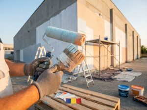 Professionele handen met verfkwasten en rollers bij commercieel gebouw met Roemeense vlagkleuren en schildersgereedschap